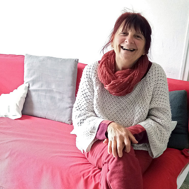 Femme souriante assise sur un canapé rouge, Mauricette, une leçon d'authenticité