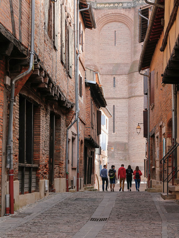 Cinq jeunes marchent dans une rue vers la cathédrale en briques roses d'Albi dans le Tarn