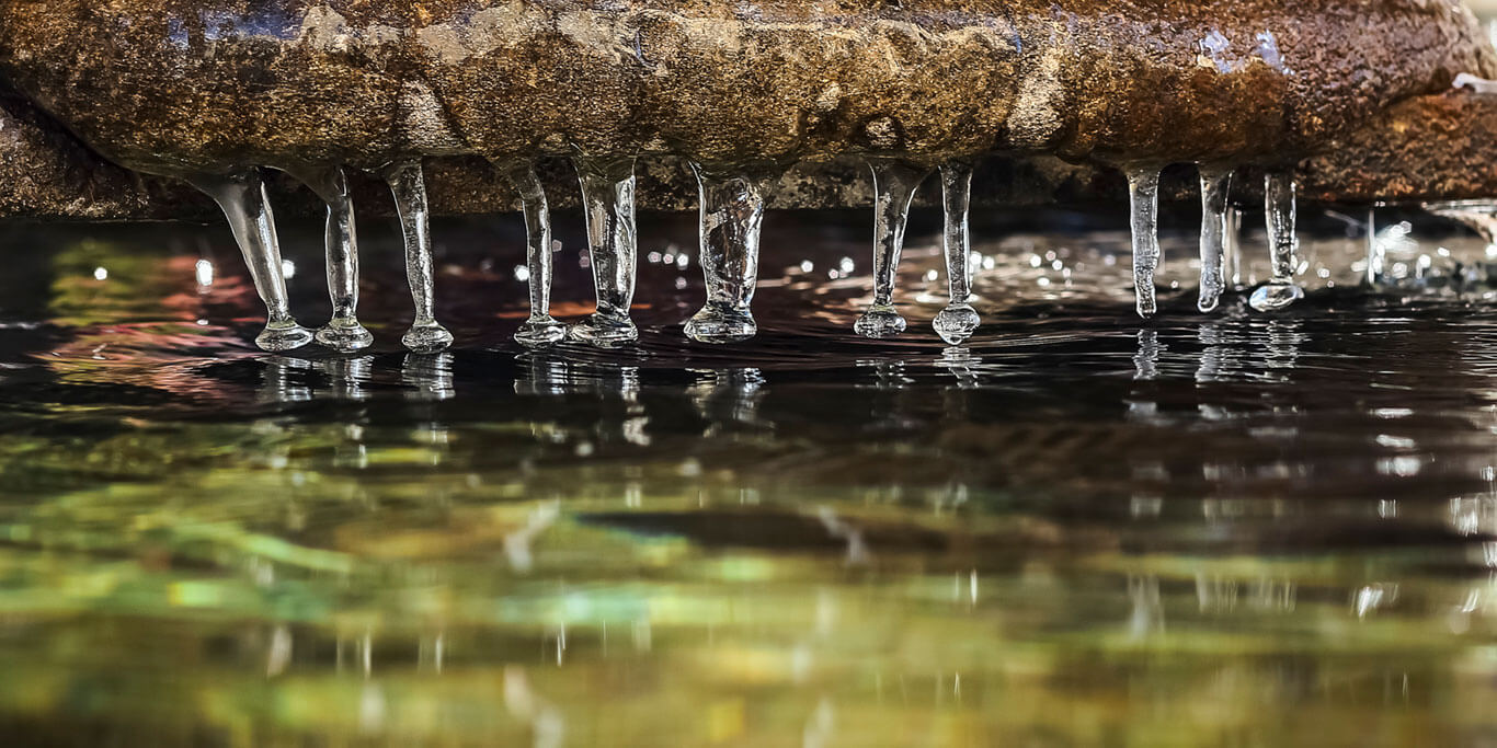 Stalactites d'eau glacée accrochées à un rocher au dessus d'un lac