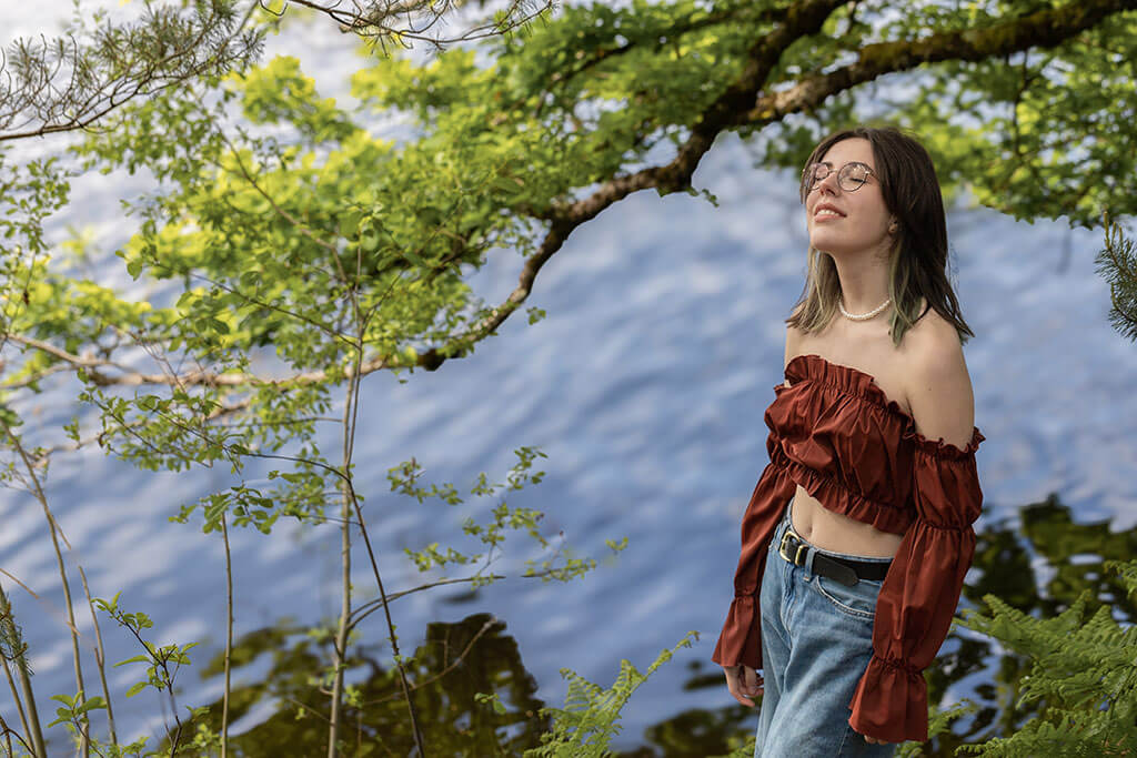 jeune-fille-sourire-lunettes-debout-arbre-lac
