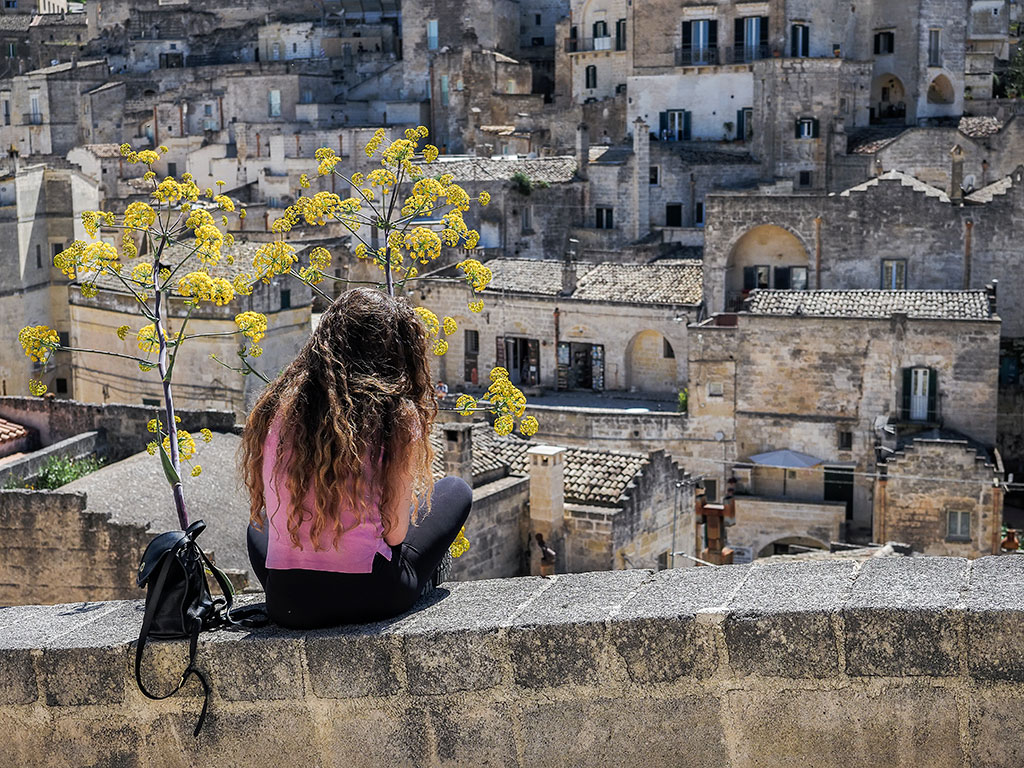 Jeune fille en rose assise sur un muret près de fleurs jaunes à Matera en Italie