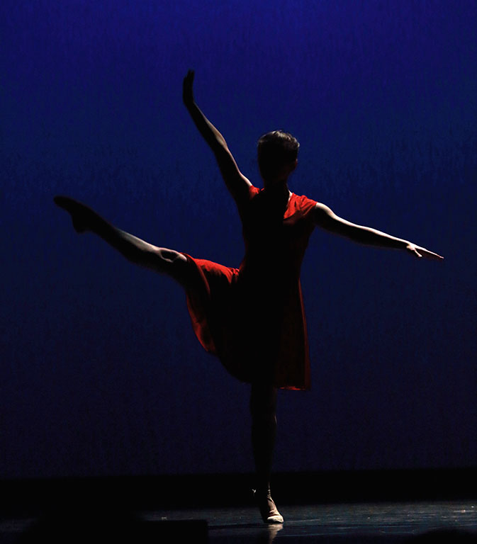 Silhouette d'une danseuse en robe rouge en équilibre sur une jambe
